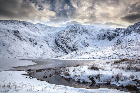 Mountain View, Cwm Idwal - Snowdonia. Snow covered mountains surround the frozen lake of Llyn Idwal with dark grey storm clouds looming above. Smart Imaging & Framing Landscape Photography