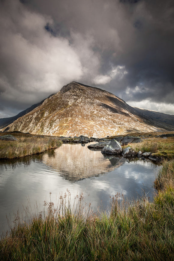 Pen yr Ole Wen, Snowdonia - An image taken from Cwm Idwal, looking towards Pen yr Ole Wen with stormy clouds above. An upright image of the mountain reflecting in the still waters of the lake. North Wales