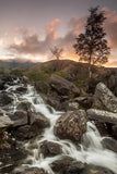 Rhaeadr Idwal, one of the most popular waterfalls in Snowdonia. Water cascades over the rocks as the orange colours of sunset fill the sky above. Snowdonia, North Wales