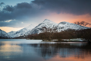 A strange looking sky at sunset over Llyn Padarn in Llanberis, Snowdonia - North Wales. Just one snow covered mountains top glows orange amongst the stormy clouds reflecting in the water below