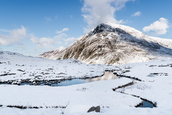 The Snowy Stream to Pen yr Ole Wen, Snowdonia - North Wales. A thick layer of snow lays on the ground at Cwm Idwal looking towards Pen yr Ole Wen with blue skies and cloud