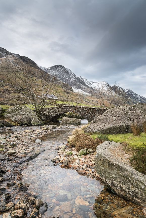 Afon Nant Peris parallels the Llanberis path as it winds its way through the mountains from Pen-y-Pass in Snowdonia, North Wales. Snow covered mountain tops below grey cloudy skies