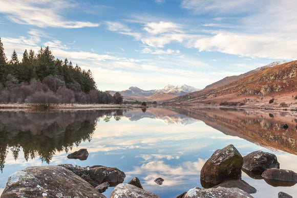 A Winter's day at Capel Curig looking along the lake of Llyn Mymbyr towards the snow covered mountains of the Snowdon Horseshoe. Beautiful reflections of the trees and hillside in the perfectly still water. North Wales