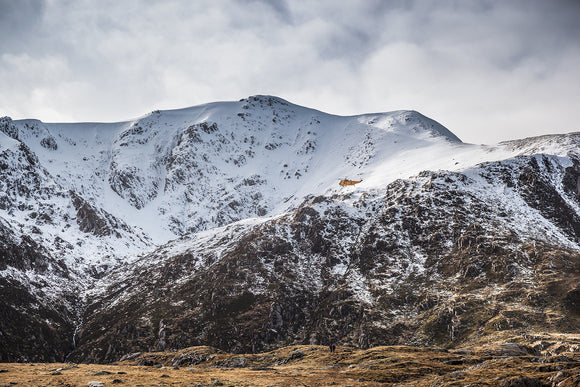 Search & Rescue - Snowdonia, North Wales. The now retired yellow RAF Seaking helicopter is dwarfed by the surrounding mountains as it flies around the snow covered mountains of Cwm Idwal.